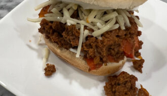 Toasted sandwich bun filled with not so sloppy joe mix, sour cream and melted white cheddar, served on a white plate.