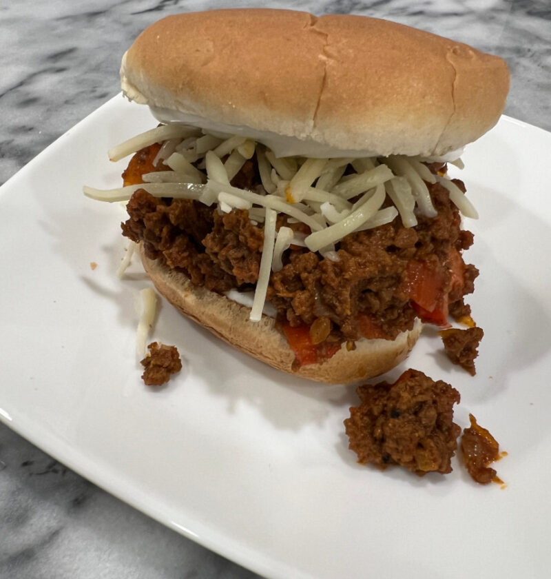 Toasted sandwich bun filled with not so sloppy joe mix, sour cream and melted white cheddar, served on a white plate.
