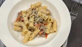 Bowl of creamy Italian chicken sausage pasta recipe with rigatoni, parmesan, lemon zest and scallions, served in a white dish.