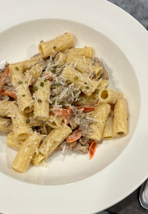 Bowl of creamy Italian chicken sausage pasta recipe with rigatoni, parmesan, lemon zest and scallions, served in a white dish.