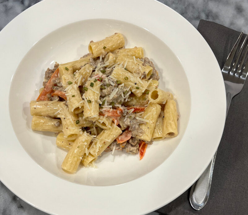 Bowl of creamy Italian chicken sausage pasta recipe with rigatoni, parmesan, lemon zest and scallions, served in a white dish.