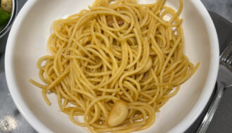 Close-up of pasta con aglio e olio served in a white bowl, featuring golden garlic slices glistening in olive oil