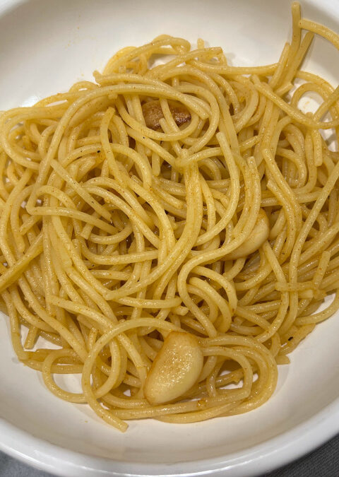 Close-up of pasta con aglio e olio served in a white bowl, featuring golden garlic slices glistening in olive oil