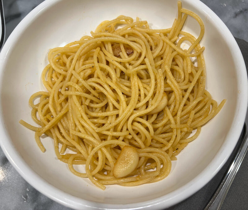 Close-up of pasta con aglio e olio served in a white bowl, featuring golden garlic slices glistening in olive oil