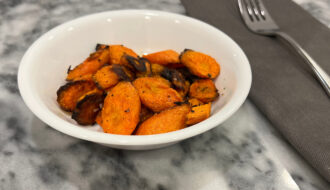 roasted carrots recipe in a white bowl next to silver fork on gray napkin