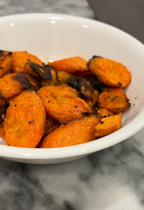 roasted carrots recipe in a white bowl next to silver fork on gray napkin
