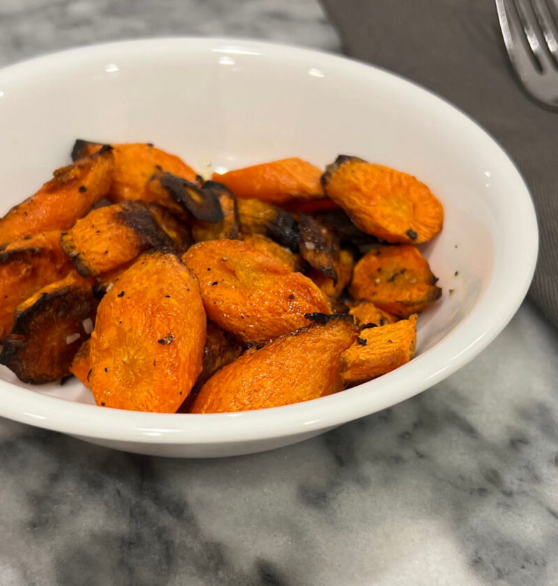 roasted carrots recipe in a white bowl next to silver fork on gray napkin