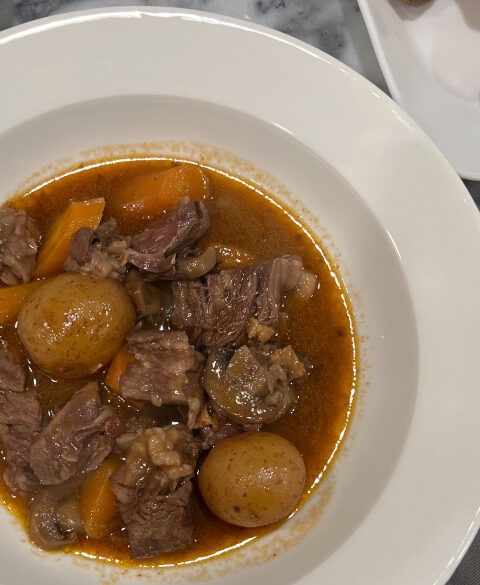 Slow cooker boeuf bourguignon served in a white bowl, featuring tender chunks of beef, carrots, baby potatoes, and mushrooms in a rich red wine sauce, garnished with parsley.