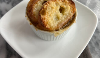Slow cooker French onion soup served in a ramekin, topped with baguette slices and melted Gruyère cheese.