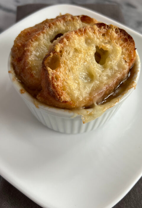 Slow cooker French onion soup served in a ramekin, topped with baguette slices and melted Gruyère cheese.