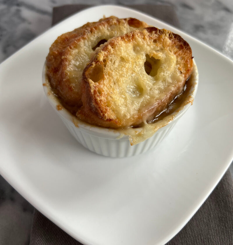 Slow cooker French onion soup served in a ramekin, topped with baguette slices and melted Gruyère cheese.