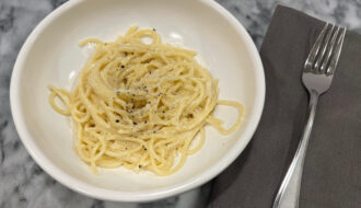 Creamy vegetarian pasta with pecorino romano cheese, served in a white bowl and topped with cracked black pepper and grated cheese
