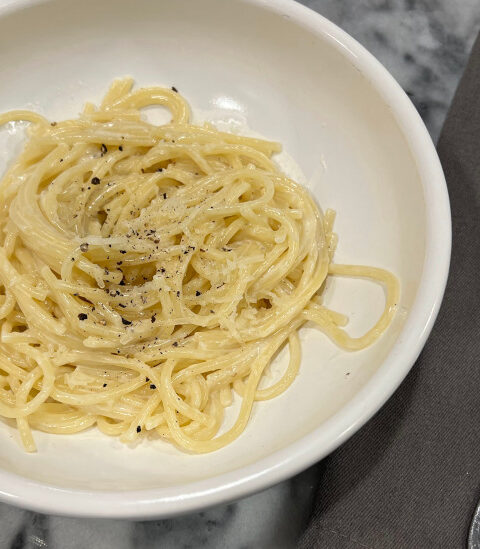 Creamy vegetarian pasta with pecorino romano cheese, served in a white bowl and topped with cracked black pepper and grated cheese