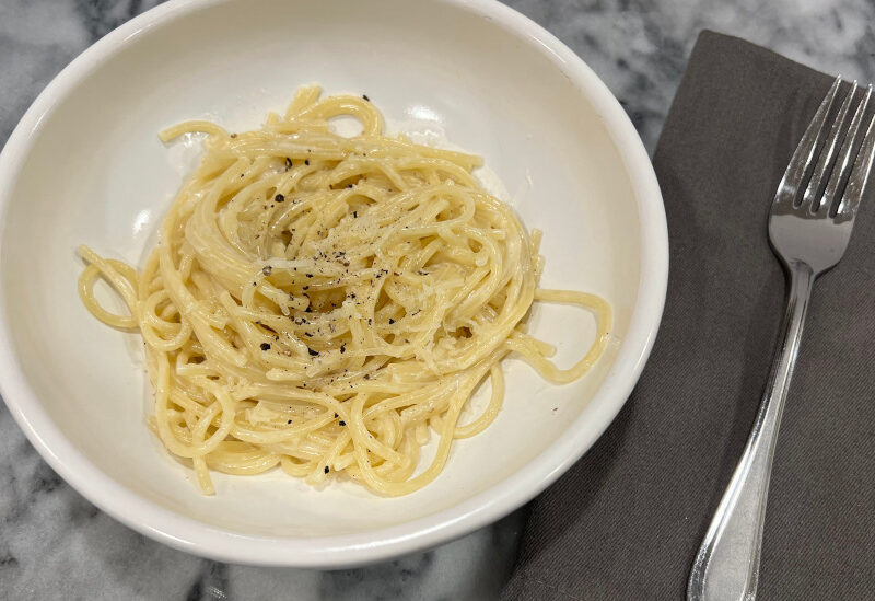 Creamy vegetarian pasta with pecorino romano cheese, served in a white bowl and topped with cracked black pepper and grated cheese