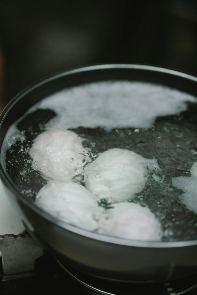 eggs boiling in water in a black pot on a stove in close up shot
