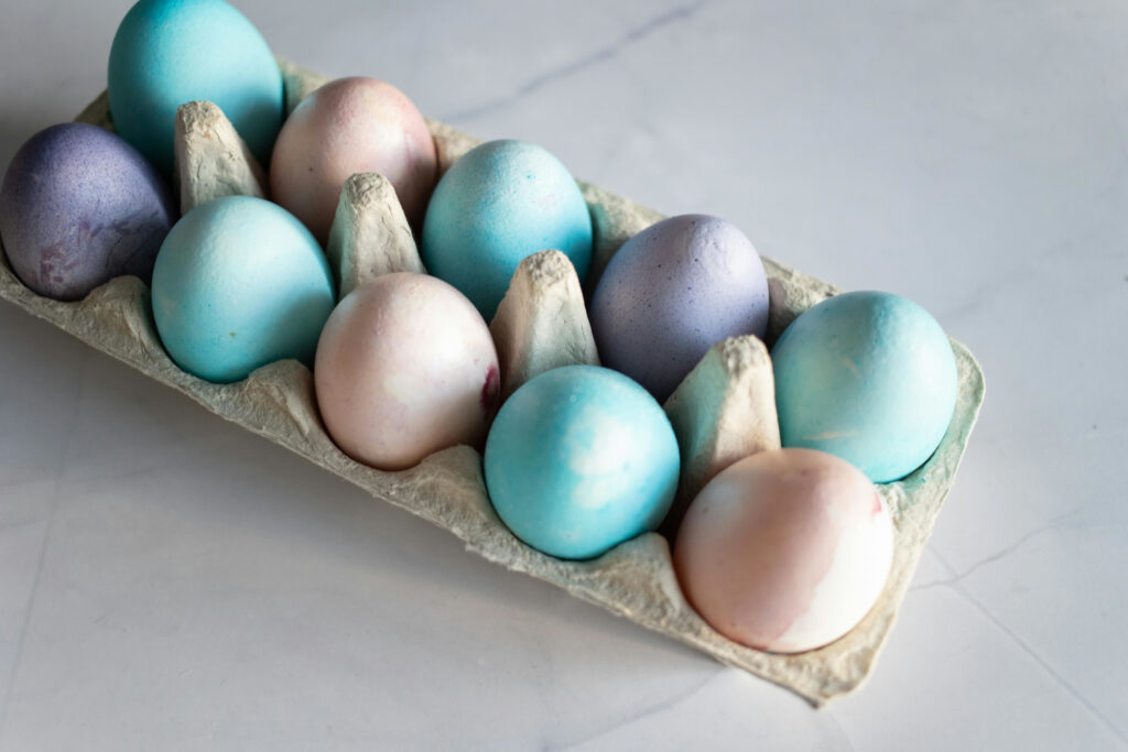 hard boiled eggs dyed light pink, light purple and light blue in a egg carton on a white background
