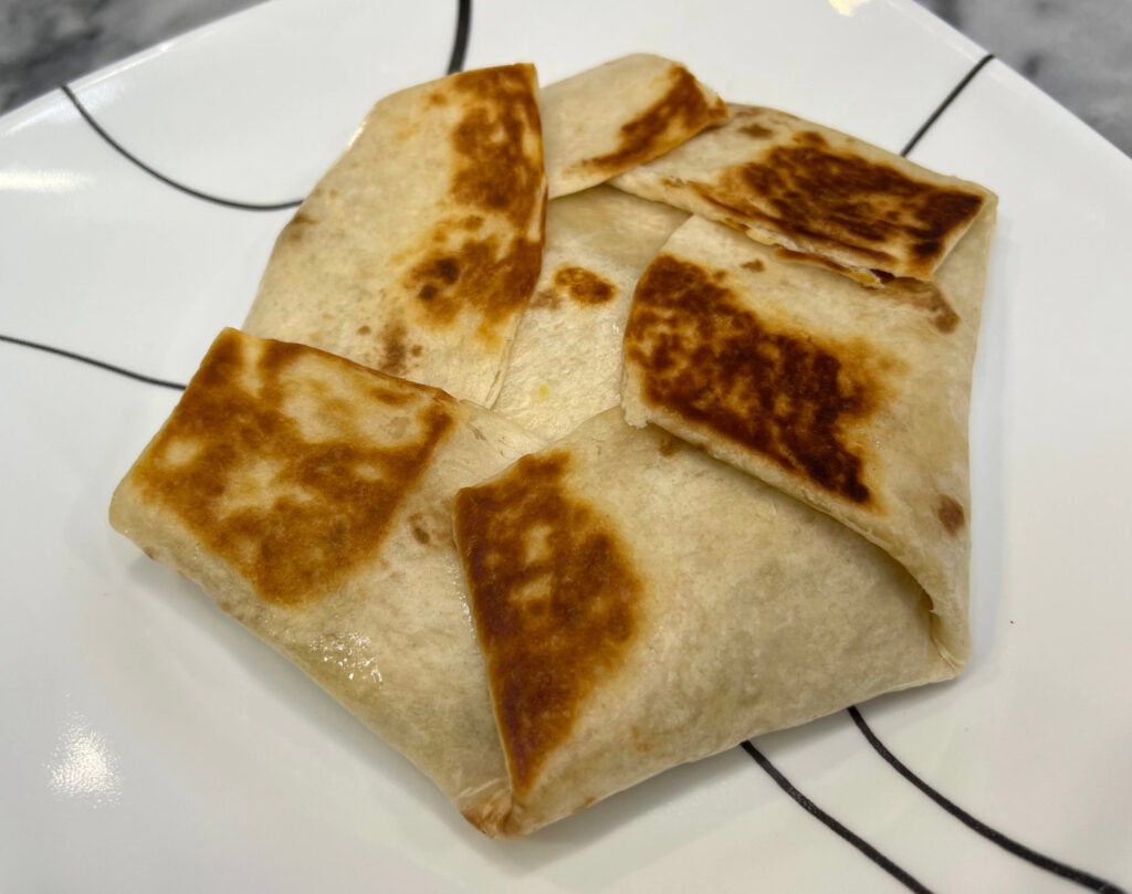 Whole vegetarian Crunchwrap Supreme on a white plate, grilled to golden brown with folded edges