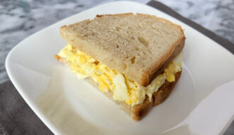 Close-up of a creamy egg salad sandwich on toasted bread, served on a white plate