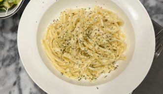 A bowl of creamy vegetarian fettuccine Alfredo topped with parsley, served with a side salad