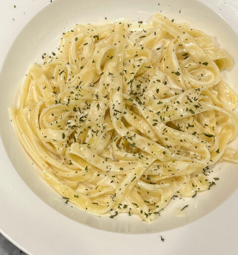 A bowl of creamy vegetarian fettuccine Alfredo topped with parsley, served with a side salad