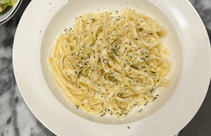 A bowl of creamy vegetarian fettuccine Alfredo topped with parsley, served with a side salad